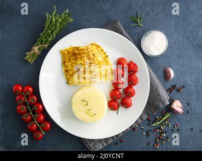 Fisch Kabeljau im Ofen mit Kartoffelpüree gebacken, Tomaten, Diät gesunde Lebensmittel. Dunkelgrauer Hintergrund Stockfoto