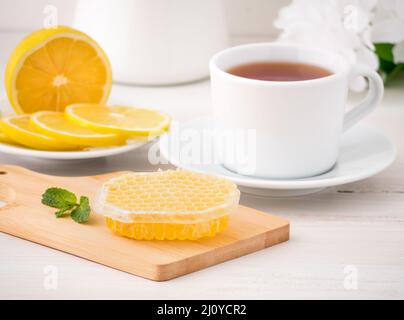 Weiße Tasse mit Tee, Zitronenscheiben und Honig in Honigwabe auf weißem Holztisch, Seitenansicht Stockfoto