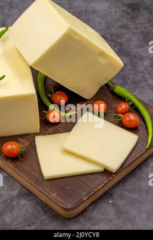 Cheddar-Käse oder Kashkaval-Käse auf dunklem Hintergrund. Käsescheiben auf dem Servierbrett Stockfoto