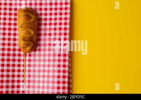 Nahaufnahme eines Maishundes mit Senfsauce auf karierter Serviette auf gelbem Hintergrund Stockfoto