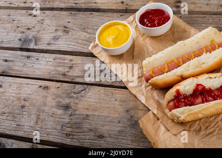 Blick auf Hot Dogs mit Tomaten und musterten Saucen auf Papiertüten am Tisch Stockfoto