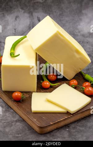 Cheddar-Käse oder Kashkaval-Käse auf dunklem Hintergrund. Käsescheiben auf dem Servierbrett Stockfoto