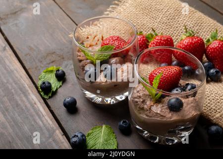 Nahaufnahme von Schokoladenmousse mit Erdbeeren, Blaubeeren und Minzblättern in Gläsern Stockfoto