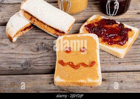 Anthropomorphe Gesicht mit Marmelade auf Brot mit Erdnussbutter von Sandwiches und Gläser auf dem Tisch gemacht Stockfoto