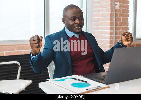 Porträt eines Afroamerikaners im Büro. Schwarzer Mann in einem Geschäftsanzug, der an einem Laptop arbeitet Stockfoto