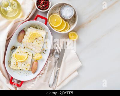 Kabeljaufischfilet, frisch im Ofen mit Zwiebeln in roter Porzellanschale zum Backen gekocht Stockfoto