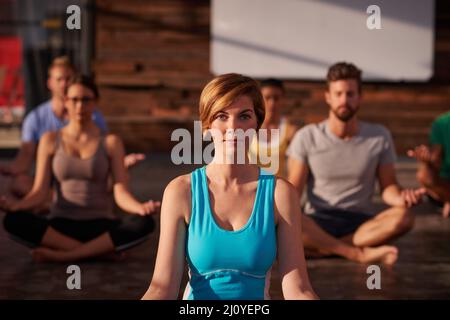 Mit Yoga geht es besser. Eine Gruppe von Menschen, die zusammen Yoga machen. Stockfoto
