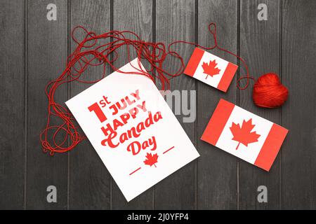 Papier mit Text 1.. JULI HAPPY CANADA DAY, Fahnen und Faden auf dunklem Holzhintergrund Stockfoto