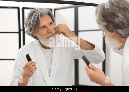 Reifer Mann, der sich im Badezimmer um seinen Bart und Schnurrbart kümmert Stockfoto