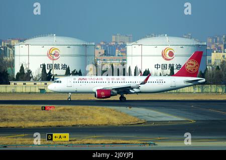 QINGDAO, CHINA - 21. FEBRUAR 2021 - Ein Passagierflugzeug der Juneyao Airlines besteuert auf der Start- und Landebahn neben dem Treibstoffspeicher der chinesischen Luftfahrt bei der Liuti Stockfoto