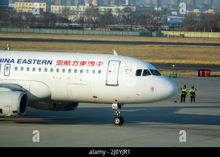 QINGDAO, CHINA - 21. FEBRUAR 2021 - zwei Flughafenmitarbeiter winken Auf Wiedersehen zu einem Passagierflugzeug, während es sich auf den Start am Flughafen Liuting in Qingdao vorbereitet, Stockfoto