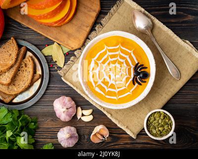 Lustiges Essen für Halloween. Kürbispüree-Suppe, Spinnennetz, dunkler alter Holztisch, Draufsicht. Stockfoto