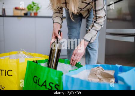 Mittelteil einer Frau, die leere Glasflaschen in den Papierkorb in der Küche wirft. Stockfoto