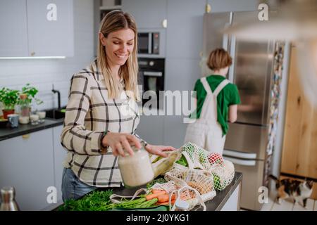 Mutter packt lokale Lebensmittel in Zero-Waste-Verpackungen aus dem Beutel in der Küche zu Hause aus. Stockfoto