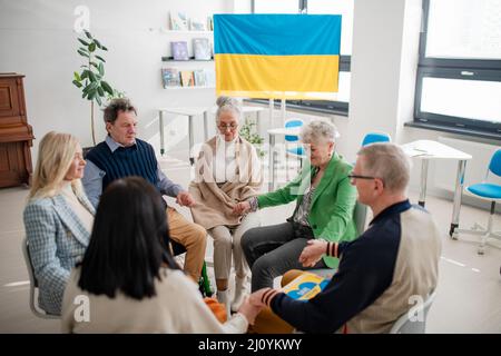 Gruppe von Senioren, die Hände halten und gemeinsam für die Ukraine im kirchlichen Gemeindezentrum beten. Stockfoto