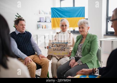 Gruppe von Senioren, die Unterstützung zeigen, wenn sie gemeinsam für die Ukraine im kirchlichen Gemeindezentrum beten. Stockfoto