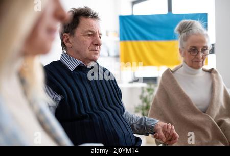 Gruppe von Senioren, die Hände halten und gemeinsam für die Ukraine im kirchlichen Gemeindezentrum beten. Stockfoto