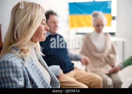 Gruppe von Senioren, die Hände halten und gemeinsam für die Ukraine im kirchlichen Gemeindezentrum beten. Stockfoto