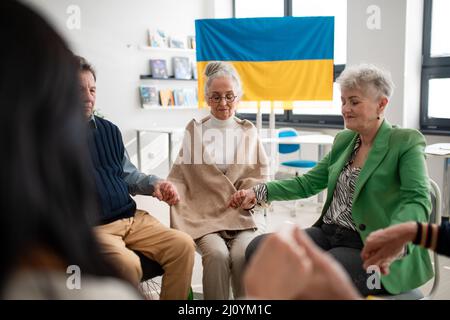 Gruppe von Senioren, die Hände halten und gemeinsam für die Ukraine im kirchlichen Gemeindezentrum beten. Stockfoto
