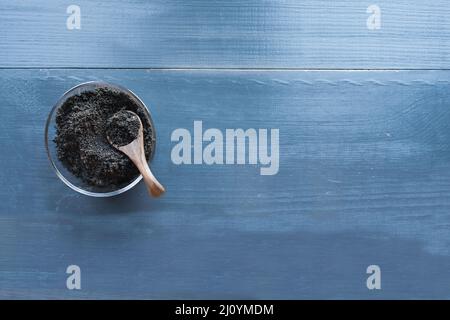 Blick von der Tischplatte auf den Kaffeesatz in einer Glasschüssel mit Holzlöffel auf einem dunkelblauen rustikalen Holzhintergrund. Biologisch nachhaltige Art zu düngen Stockfoto