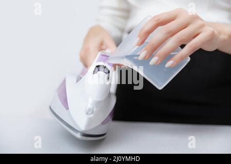 Nahaufnahme einer Schneiderin, die Wasser in das Dampfbügeleisen gießt. Stockfoto