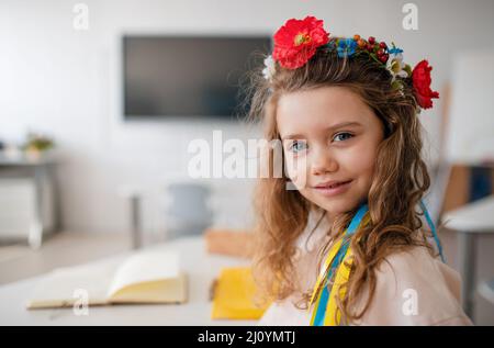 Kleines glückliches ukrainisches Mädchen, das im Klassenzimmer die Kamera anschaut, Konzept der Einschreibung ukrainischer Kinder in Schulen. Stockfoto