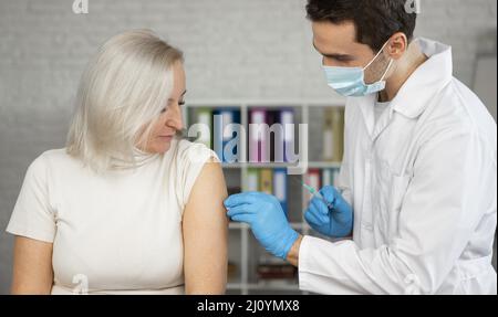 Arzt mit mittlerer Schussaufnahme, der den Impfstoff verabreicht. Hochwertige Fotos Stockfoto