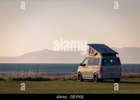 Ein Volkswagen Wohnmobil mit seinem Dach am Strand von Barassie in der Nähe von Troon, Ayrshire, Schottland, Großbritannien, genießt die wärmenden Strahlen, wenn die Sonne über der Isle of Arran untergeht. Kredit: Windmill Images/Alamy Live Nachrichten Stockfoto