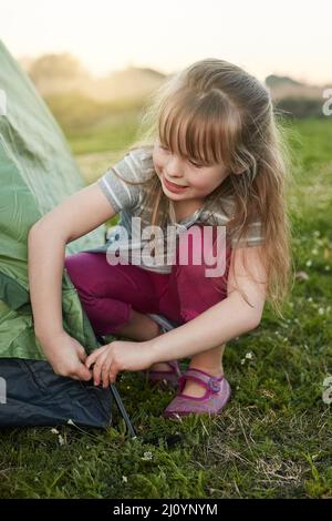 Rufen Sie mich einfach den Lagermeister an. Eine kurze Aufnahme eines kleinen Mädchens, das alleine ein Zelt aufstellt. Stockfoto