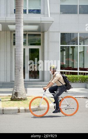 Junger Mann mit Helm und medizinischer Maske beim Fahrradfahren in der Stadt Stockfoto