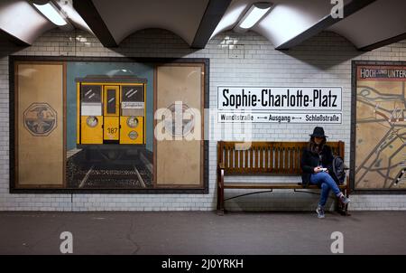 Mädchen/Frau sitzt auf einer Bank am U-Bahnhof Sophie Charlotte Platz in Berlin Stockfoto