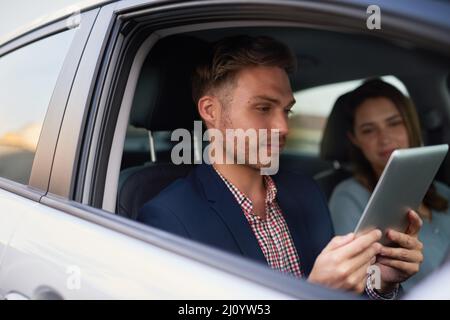 Die intelligenteste Route finden. Aufnahme eines jungen Mannes, der mit seiner Frau in einem Auto auf ein Tablet schaut. Stockfoto