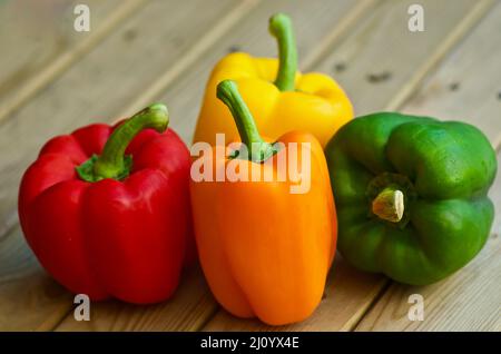 Nahaufnahme von vier Paprika in verschiedenen Farben, die im Sommer auf einem Holztisch im Freien liegen. Stockfoto