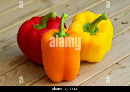 Nahaufnahme von drei Paprika in verschiedenen Farben, die im Sommer auf einem Holztisch im Freien liegen. Stockfoto