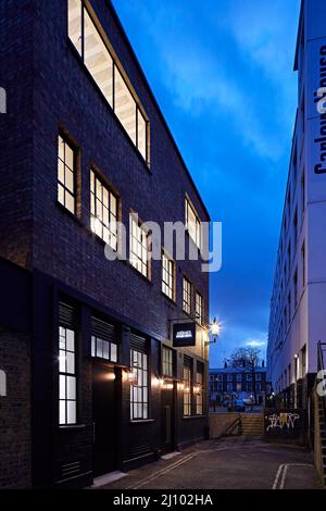 Blick entlang der Gebäudefassade in der Dämmerung. Symes Mews, London, Großbritannien. Architekt: PH+ Architects, 2020. Stockfoto