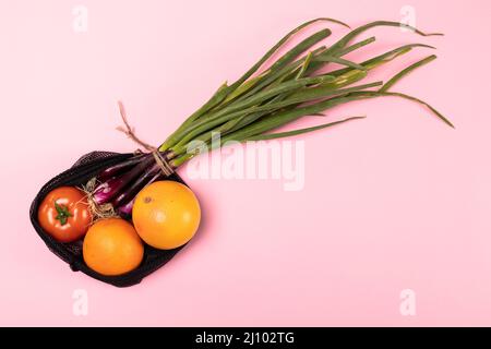 Direkt über Schuss von Orangen mit Tomaten und Frühlingszwiebel in schwarzem Netz auf rosa Hintergrund Stockfoto