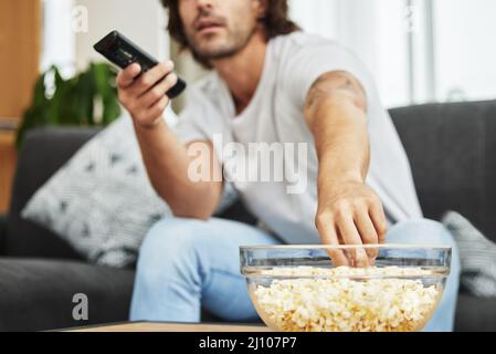 Ich konnte diese ganze Schüssel essen, ohne dass jemand zuschaute. Aufnahme eines Mannes, der auf der Couch saß und Popcorn aß und fernsah. Stockfoto