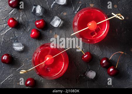 Cocktails mit Kirschen und Eis, darüber liegende flache Lay Shot. Alkoholgetränke auf schwarzem Schieferhintergrund Stockfoto