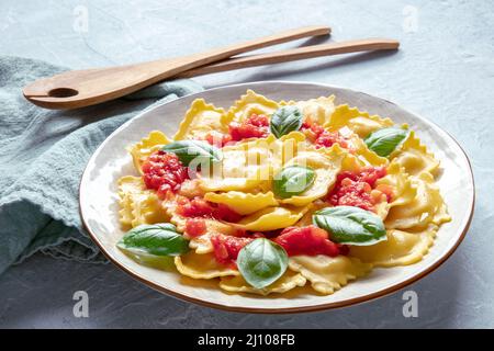Ravioli mit Tomatensauce und frischen Basilikumblättern, italienisches Rezept, auf Schieferboden mit einem Holzlöffel Stockfoto
