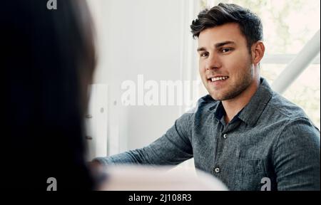 Ergebnisse zu sehen macht mich glücklich. Ausgeschnittene Aufnahme eines hübschen jungen Geschäftsmannes, der tagsüber mit einem Kollegen im Büro sitzt. Stockfoto