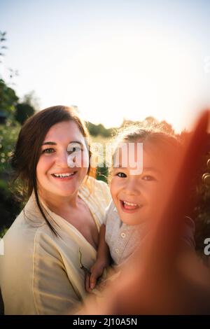 Die europäische Mutter und ihre asiatische Tochter im Sommer im Apfelgarten Stockfoto