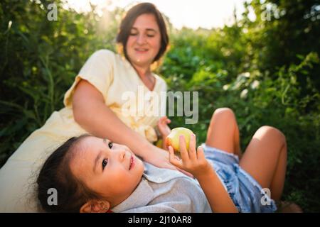 Die europäische Mutter und ihre asiatische Tochter im Sommer im Apfelgarten Stockfoto