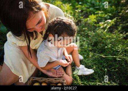 Die europäische Mutter und ihre asiatische Tochter im Sommer im Apfelgarten Stockfoto