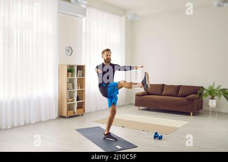 Männlicher Athlet, der während seines Fitness-Trainings zu Hause eine Beinschwingen-Sportübung macht Stockfoto