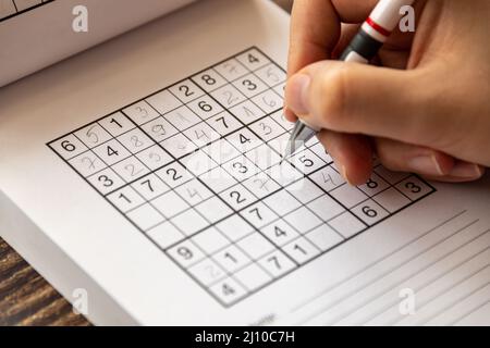 Person, die ein Sudoku-Puzzle auf einem Holztisch löst Stockfoto