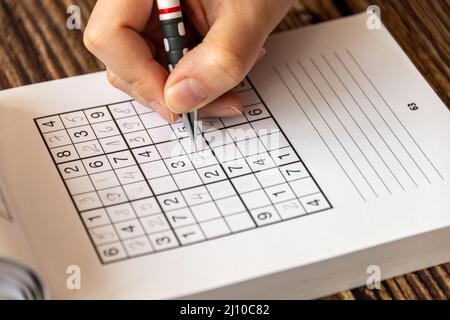 Person, die ein Sudoku-Puzzle auf einem Holztisch löst Stockfoto