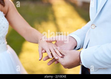 Ich möchte den Rest meines Lebens mit euch verbringen. Ausgeschnittene Aufnahme eines Bräutigams, der einen Ring auf den Finger seiner Braut legt. Stockfoto