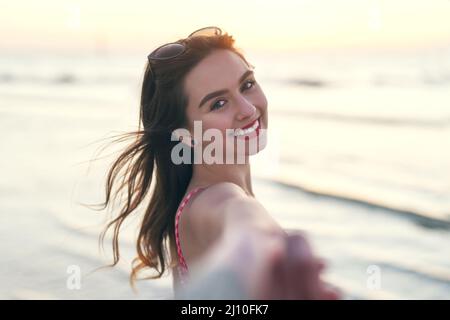 Lasst uns ins Meer gehen und frei sein. POV-Aufnahme einer schönen jungen Frau, die ihre besten Freundinnen am Strand in der Hand hält. Stockfoto