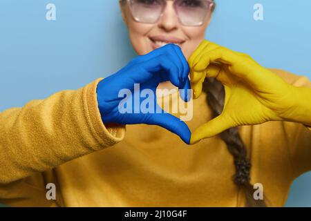 Porträt eines Mädchens mit Herzform Ukrainische gelbe und blaue Flagge auf den Händen bilden ein Herz. Unterstützung der Ukraine Stockfoto