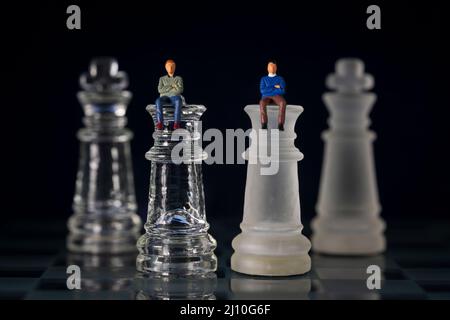 Miniatur-Geschäftsleute 2 Menschen sitzen auf Königin Schach Stück Könige auf dem Rücken verhandeln im Geschäft Stockfoto